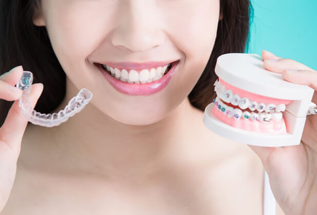 person holding an Invisalign aligner and a model of a mouth with braces 