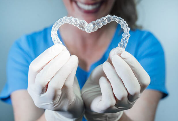 dental hygienist holding two Invisalign aligners in the shape of a heart 